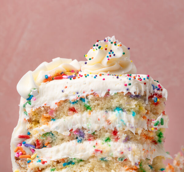 Slice of funfetti cake with sprinkles on the sides and on top of the cake.